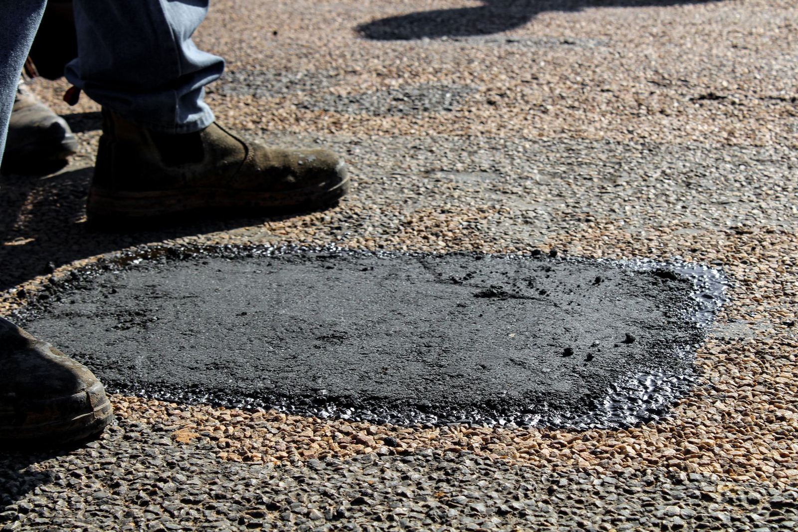 Worker performing asphalt patching repair on pavement