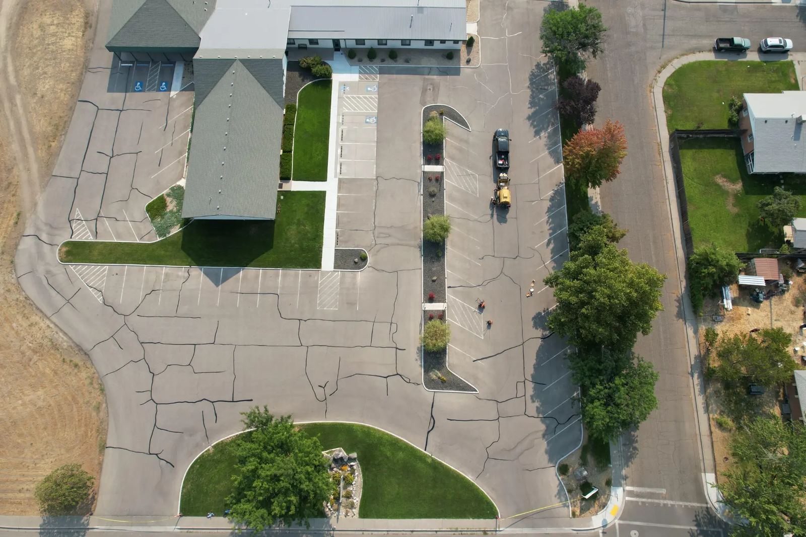 Aerial view of a church parking lot before sealcoating, showing heavy cracking and faded striping