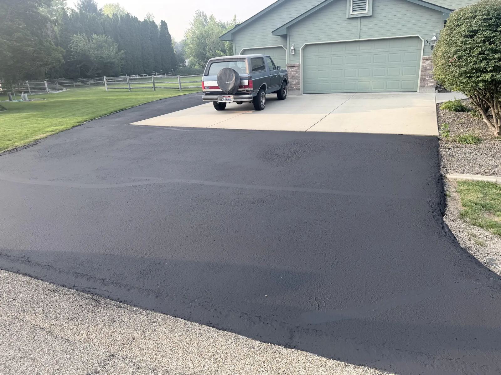 Residential driveway apron freshly sealcoated up to the concrete pad by Supreme Seal Coat